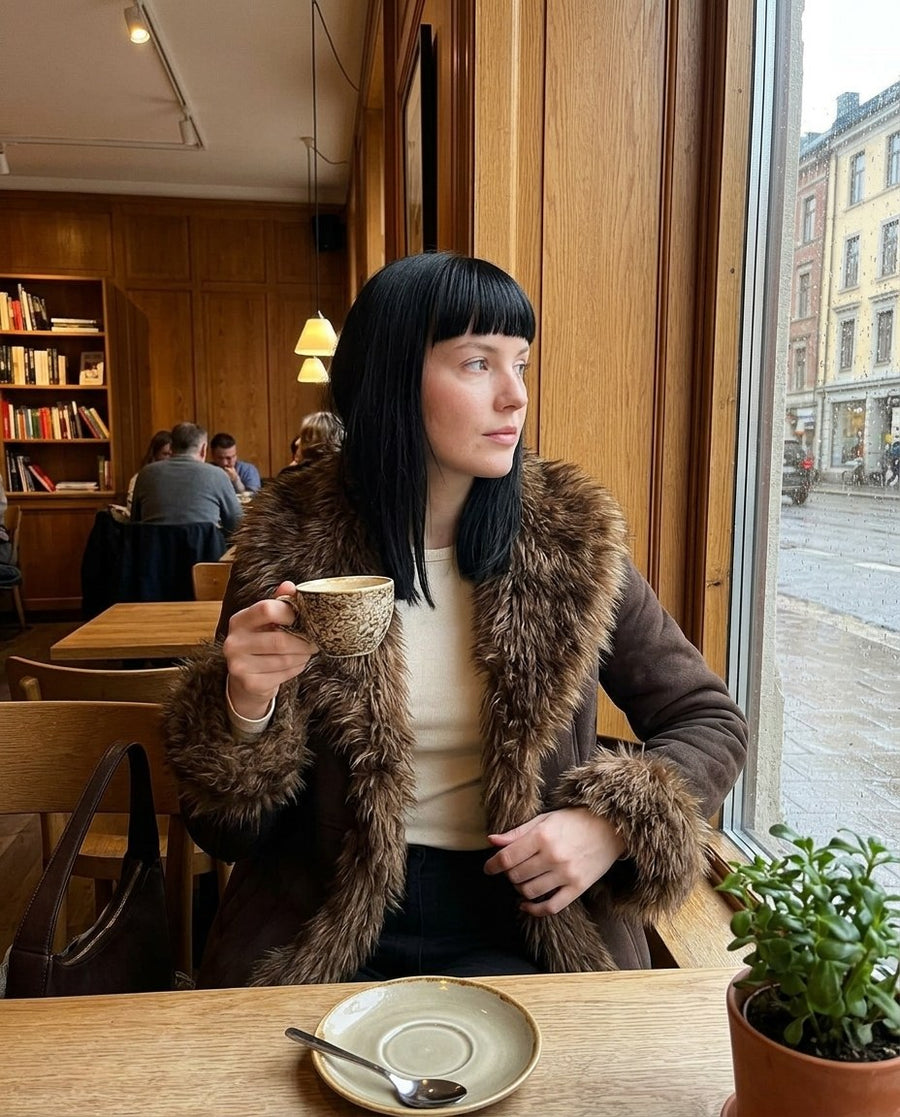 Nora, damjacka i mockalook med fuskpälskant i brun, stylinginspiration på ett kafé