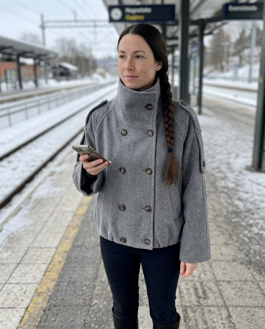 Gråmelerad jacka med hög krage på en snöig perrong
