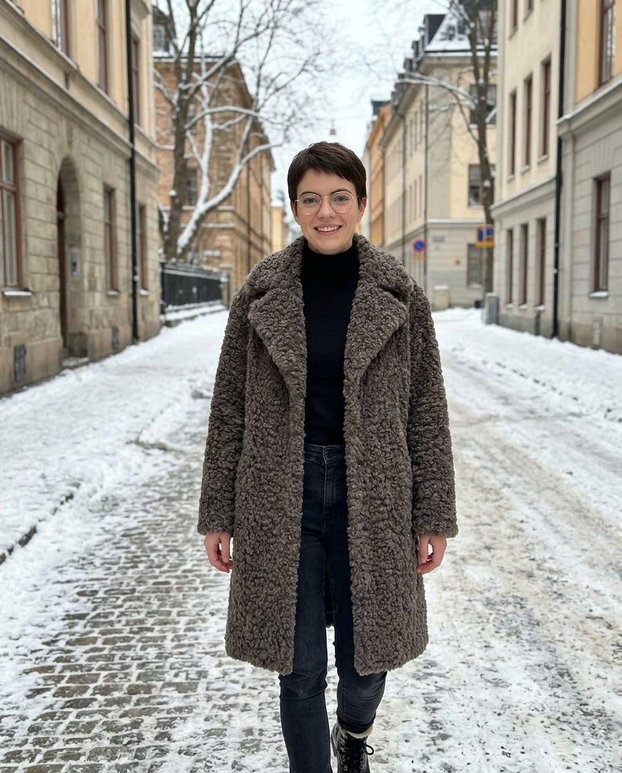 Alma, knälång kappa i lockig fuskpäls för dam i grå, stylinginspiration på en snöig gata
