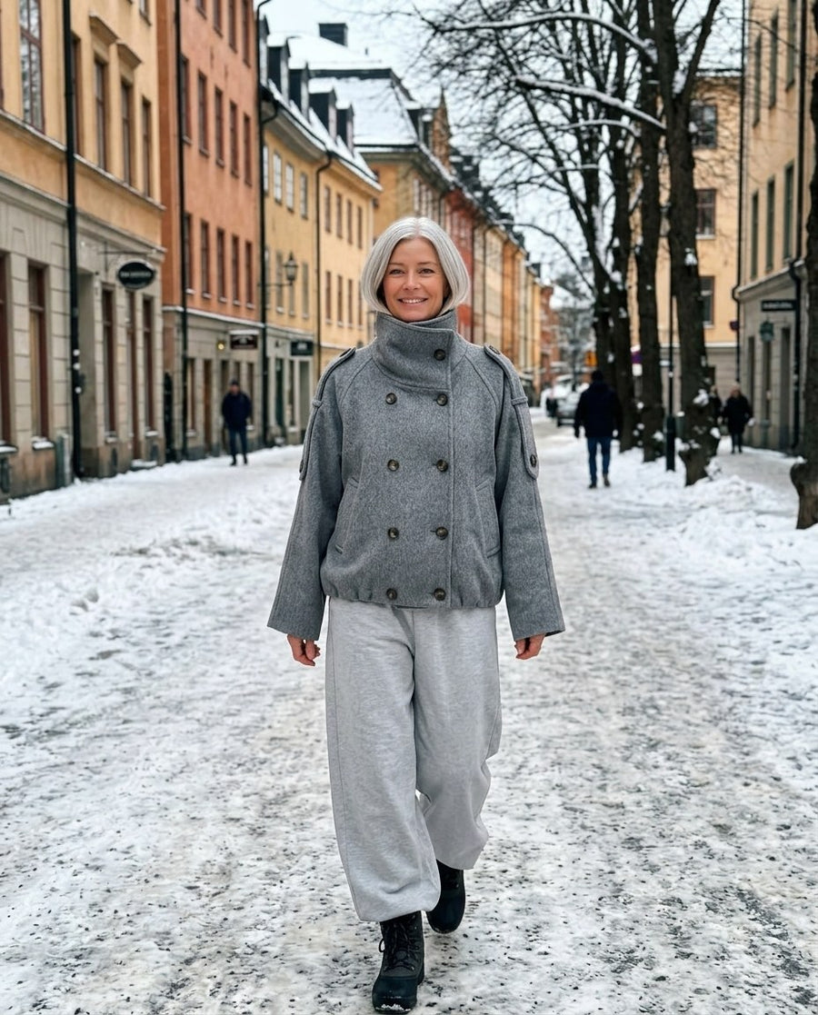 Kort grå jacka och ljusa byxor på en snöig gata