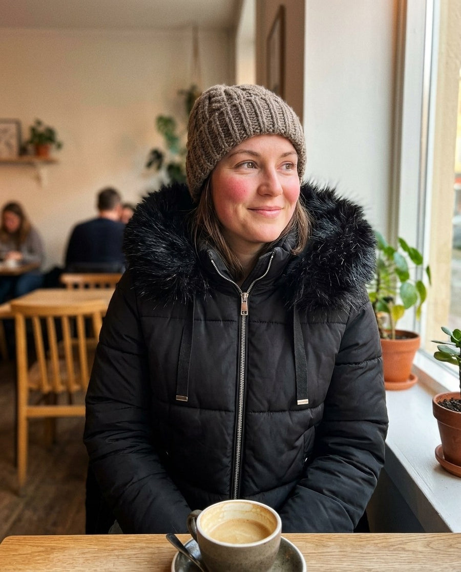 Ida, kort pufferjacka med fuskpälshuva för dam i svart, stylinginspiration på ett kafé