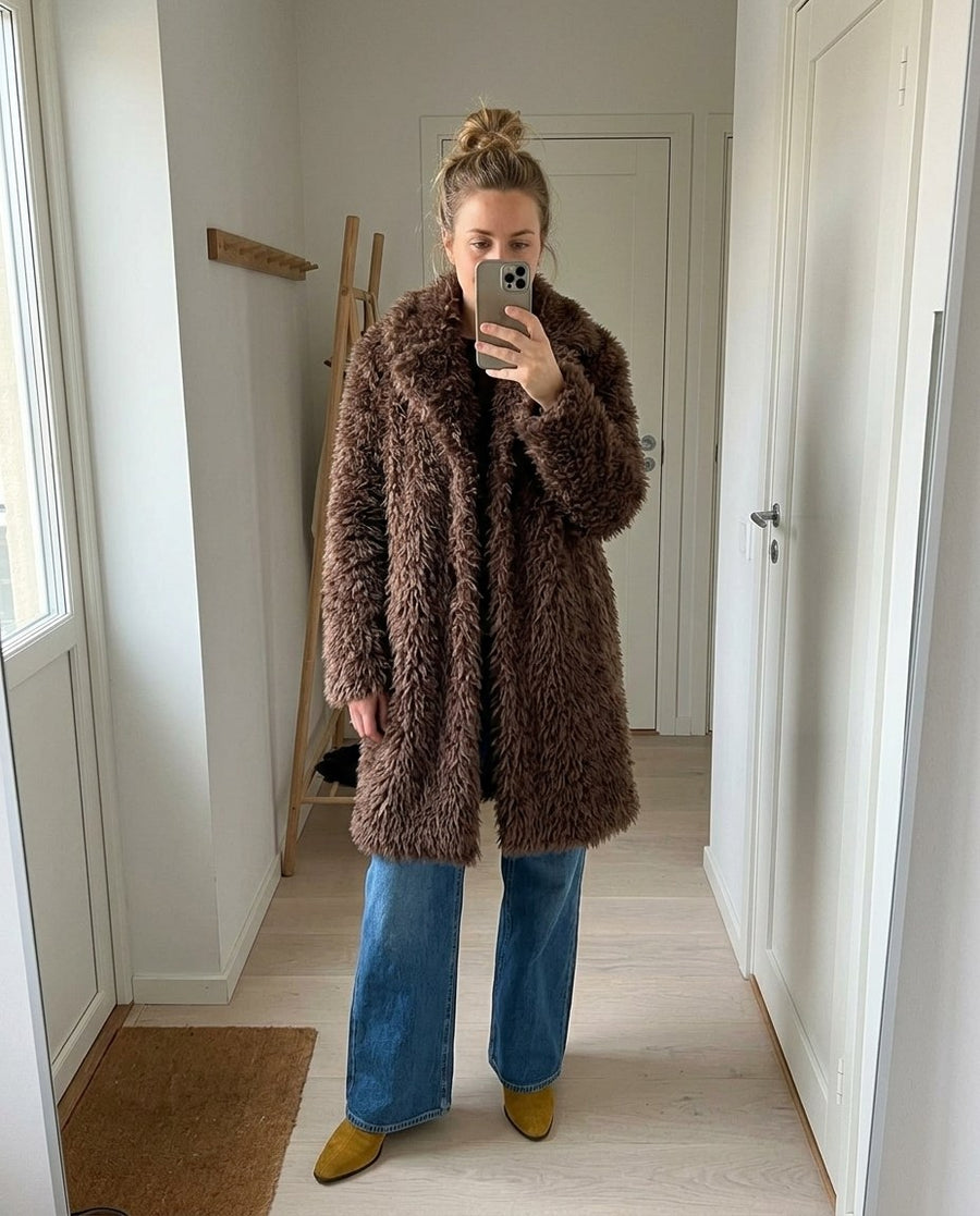 Saga, lång fuskpälskappa för dam i brun, stylinginspiration spegelbild i hallen