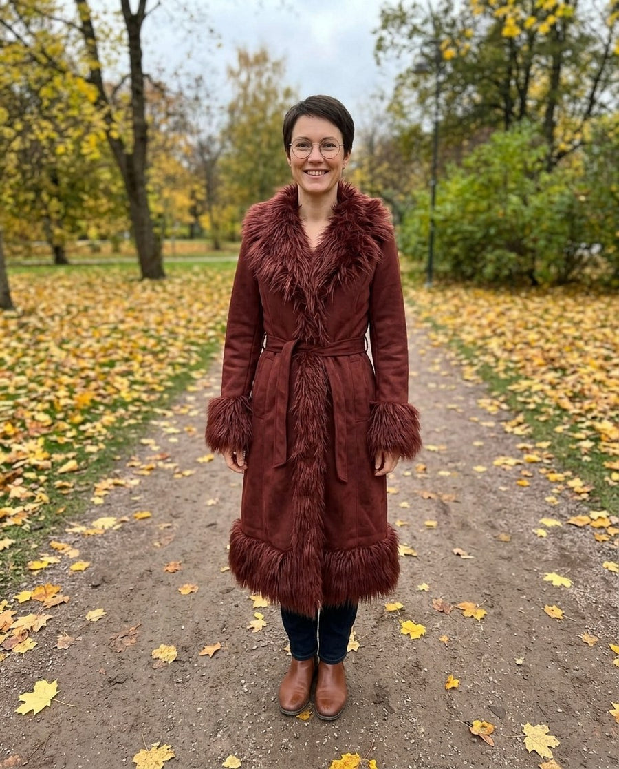 Lova, lång kappa i mockaimitation med fuskpälskant för dam i rödbrun, stylinginspiration i en höstpark