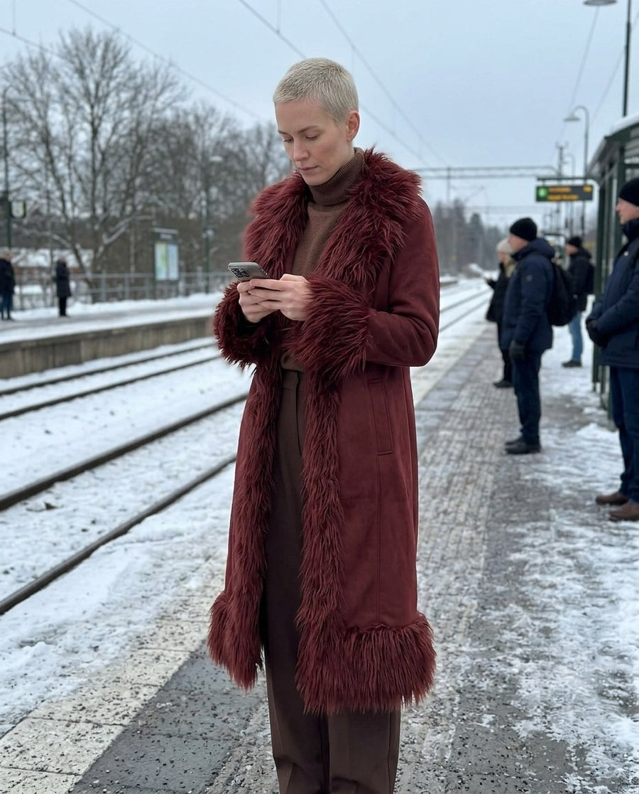 Lova, lång kappa i mockaimitation med fuskpälskant för dam i rödbrun, stylinginspiration på en perron