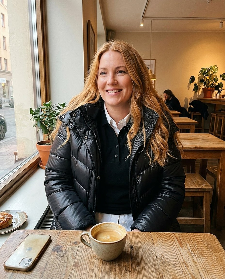 Vera, lång pufferkappa med huva för dam i svart, stylinginspiration på ett kafé