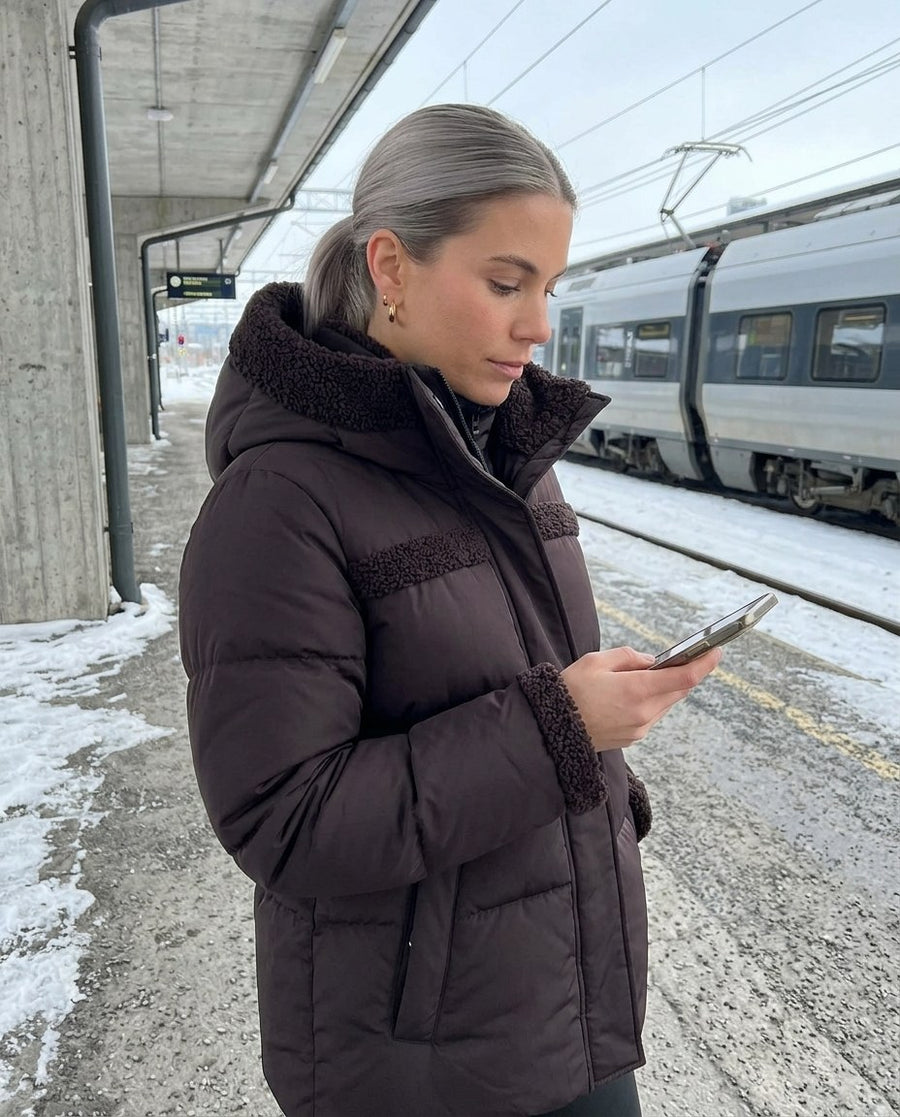 Signe, vadderad 2-i-1-jacka med huva för dam i mörkbrun, stylinginspiration på en perron