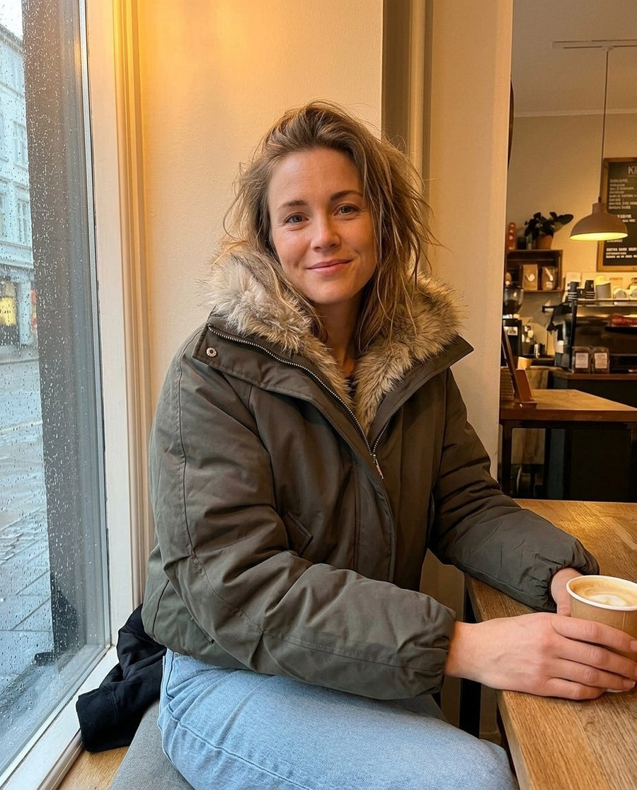 Svea, vadderad bomberjacka med hög krage för dam i mörk olivgrön, stylinginspiration på ett kafé